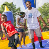 A man and three children play in a brightly colored bouncy house at a Boys & Girls Clubs event at Penn Park