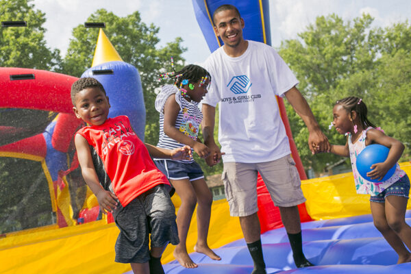 A man and three children play in a brightly colored bouncy house at a Boys & Girls Clubs event at Penn Park
