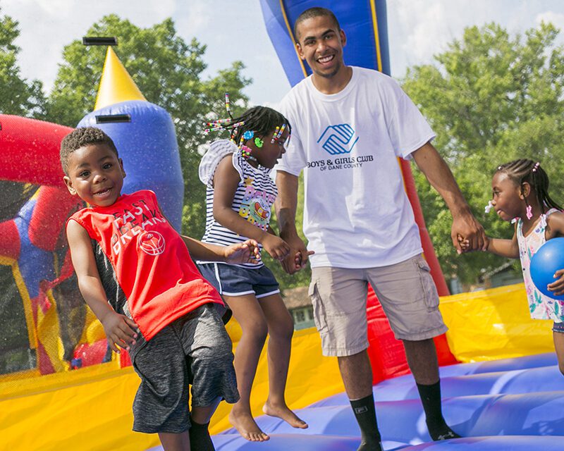 A man and three children play in a brightly colored bouncy house at a Boys & Girls Clubs event at Penn Park