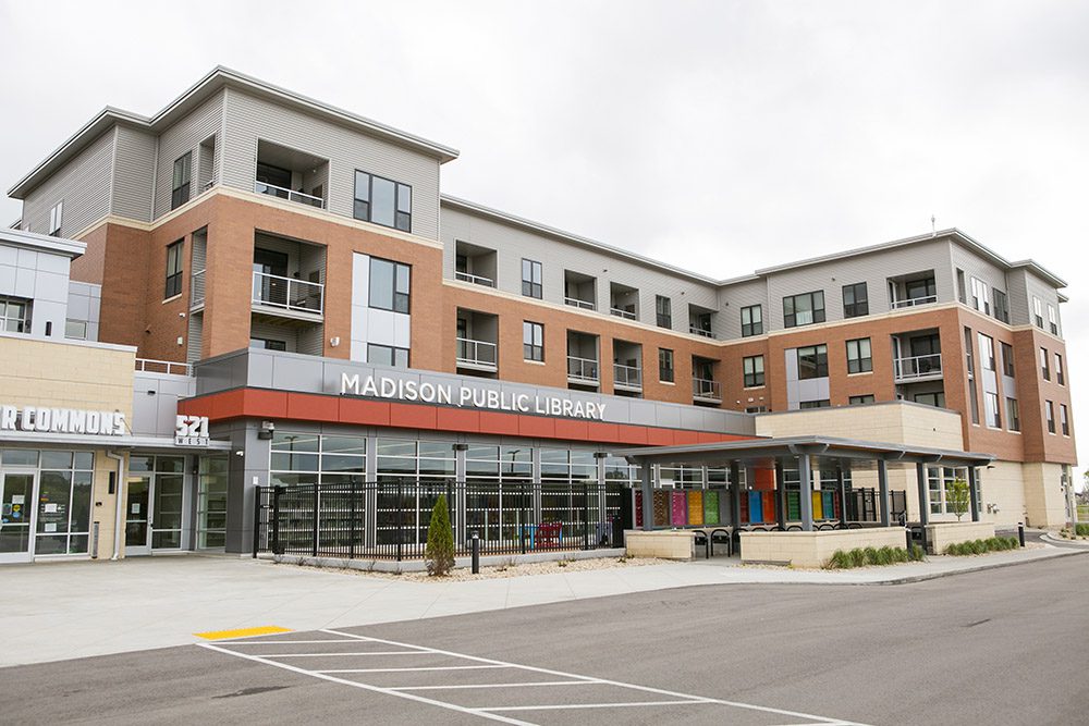 Exterior photo of the Pinney Library -- which anchors a new three-story mixed use building and features large windows and a covered patio.