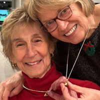 hoto of two smiling women showing off their matching necklaces