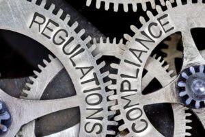 Macro photo of gears with interlocking teeth, with REGULATIONS, COMPLIANCE on them