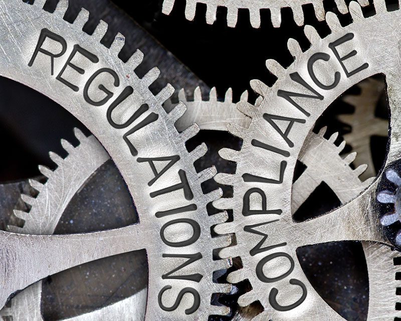 Macro photo of gears with interlocking teeth, with REGULATIONS, COMPLIANCE on them