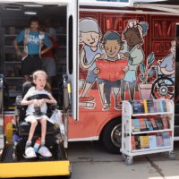 A child in a wheel chair is lifted into a mobile library that is pained with images of children reading books