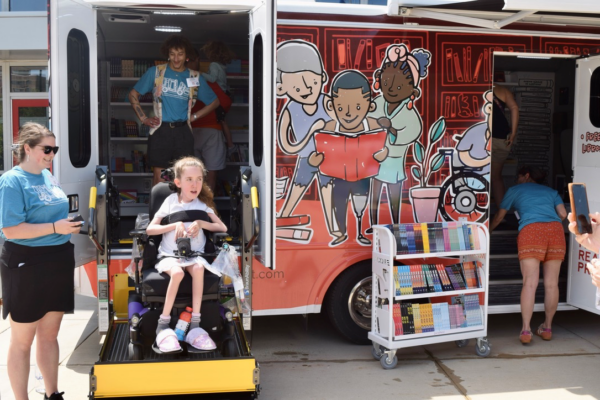 A child in a wheel chair is lifted into a mobile library that is pained with images of children reading books