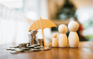 three wooden figures standing under an umbrella next to a stack of coins