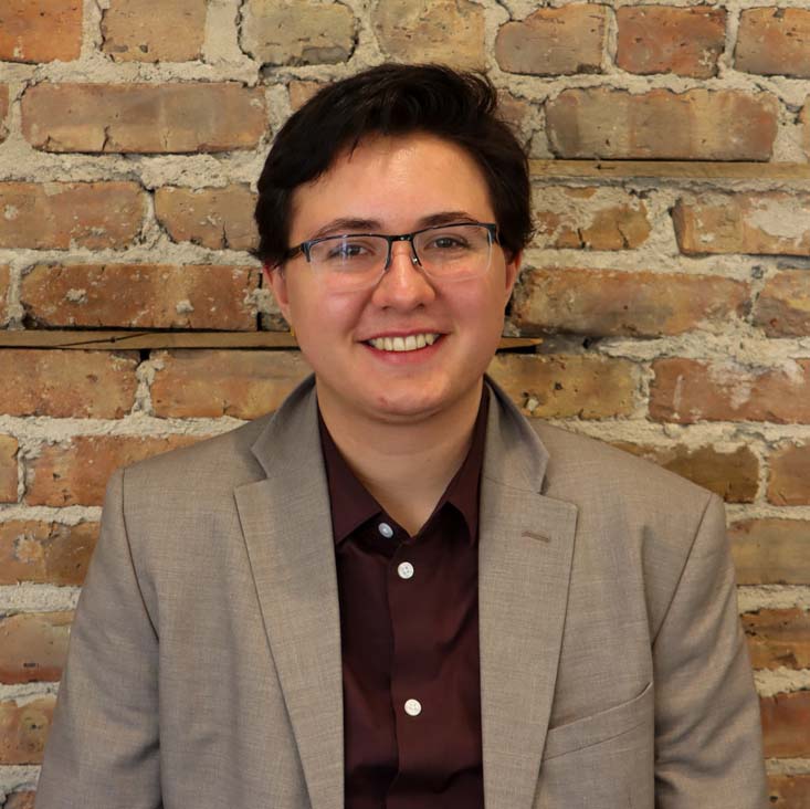 Headshot of Lex Page standing in front of a brick wall at MCF's offices