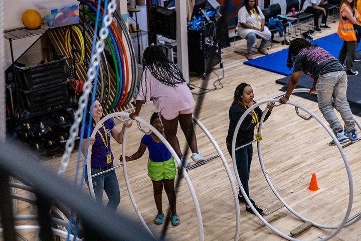 Two young children balance atop a pair of German Wheels held by instructors at Madison Circus Space