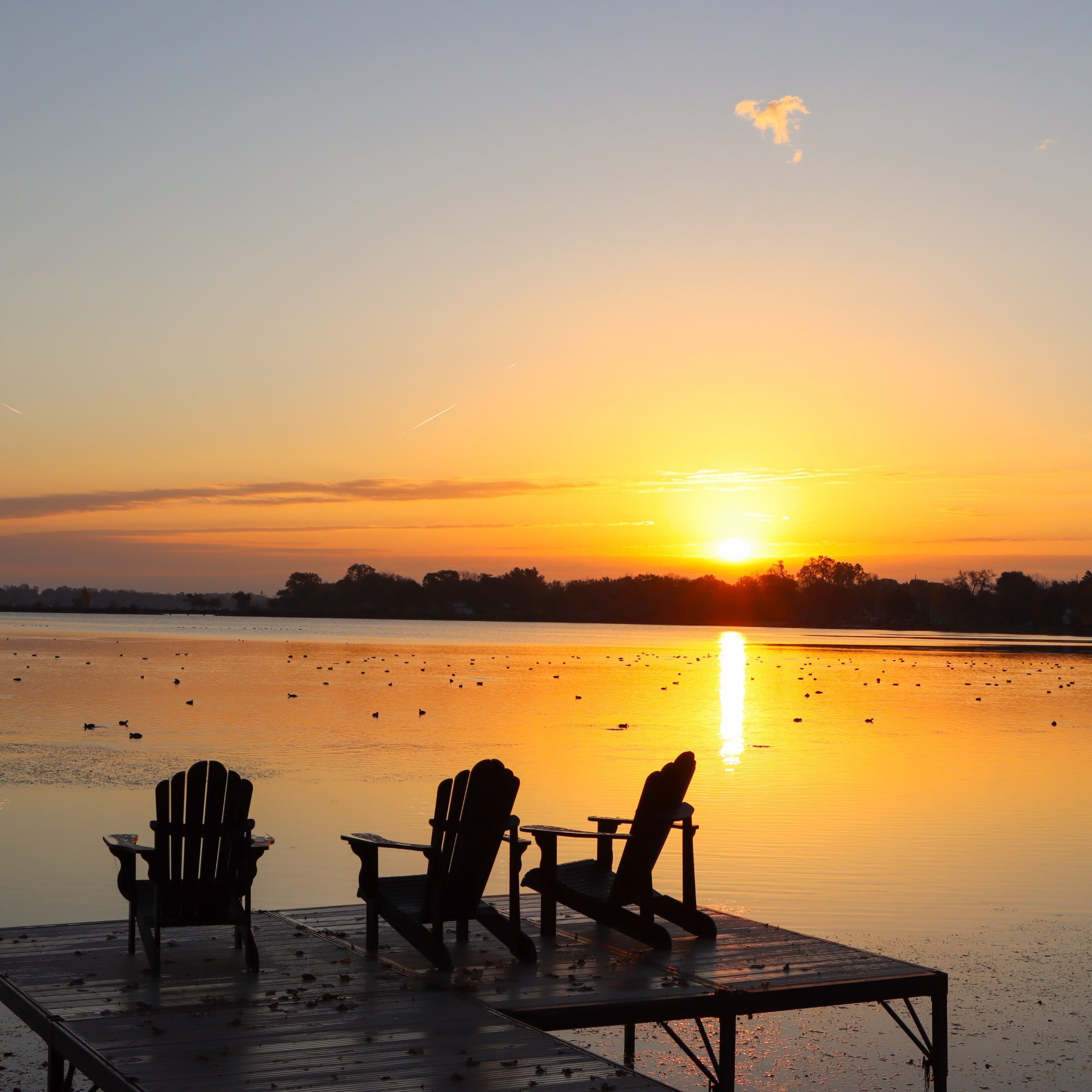 Three chairs on a dock overlooking Monona bay at sunrise