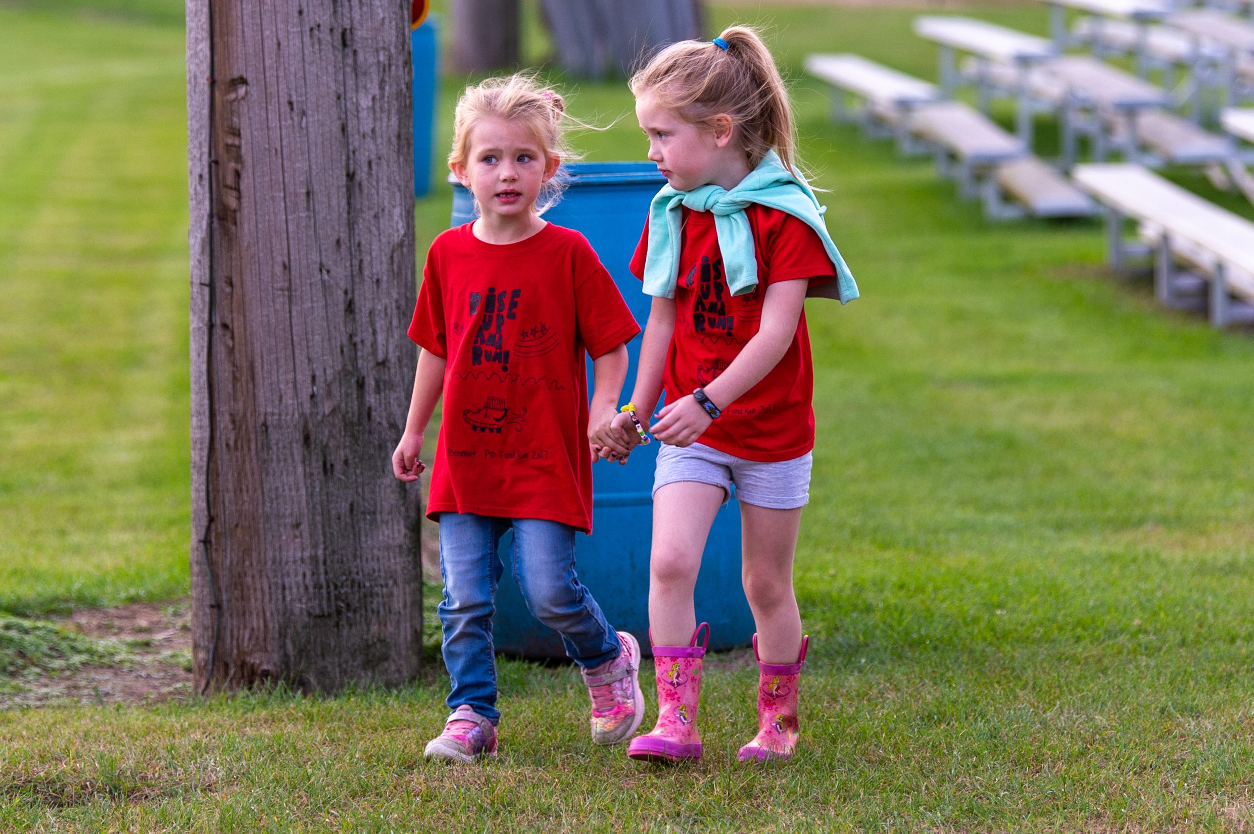 Two little girls walk hand in hand wearing matching red shirts