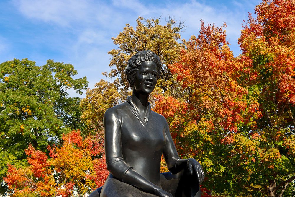 Photo of a sculpture of former Wisconsin Secretary of State Velvalea Phillips at the Wisconsin State Capitol with colorful fall foliage in the background