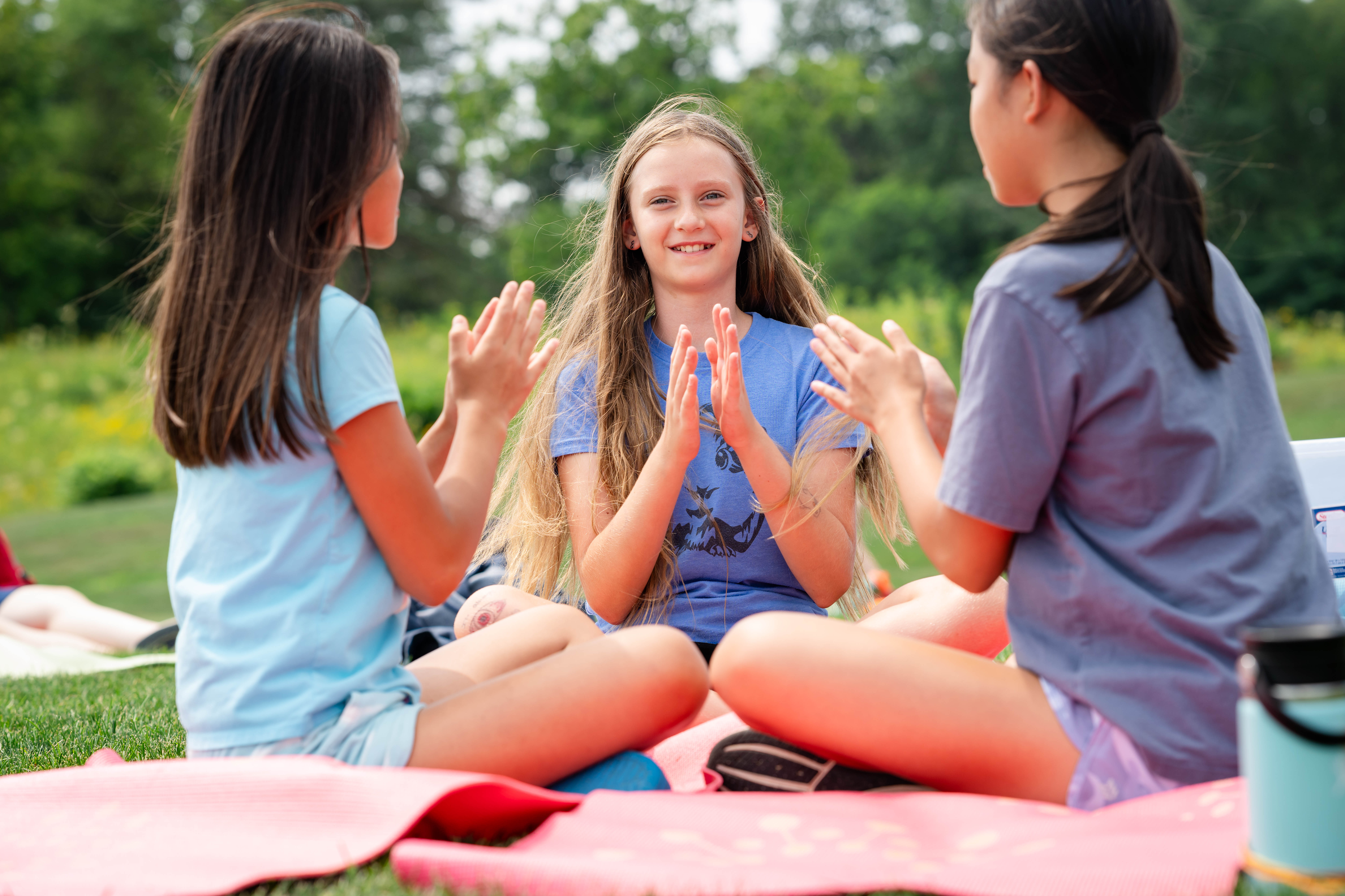 three girls sit on a blanket and play patty cake