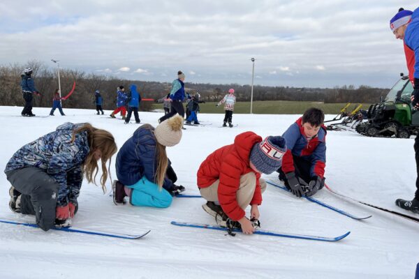 Students putting on skis with their instructor watching