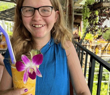 Young girl with glasses smiles as she holds a tall yellow drink with a flower in it