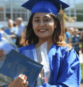 Woman in blue graduation gown holding flowers and program.