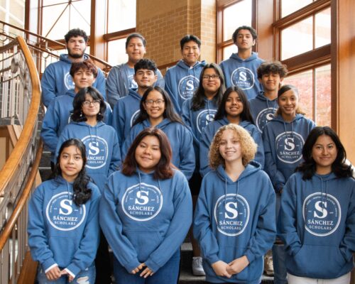 Group of students pose on staircase all wearing matching blue hoodies