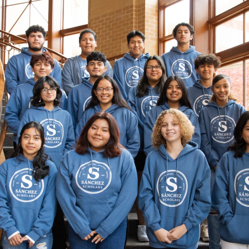 Group of students pose on staircase all wearing matching blue hoodies