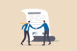 Two men shake hands in front of a signed paper that says 'Agreement'
