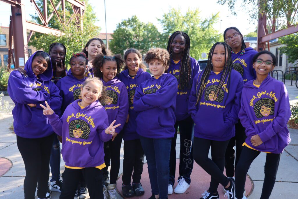 A group of girls posing with matching purple hoodies that read "Black Girl Magic"