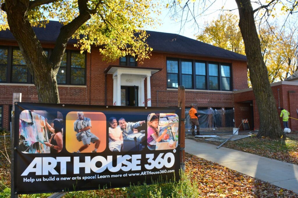 An old brick building surrounded by trees with a banner outside that reads "Art House 360"